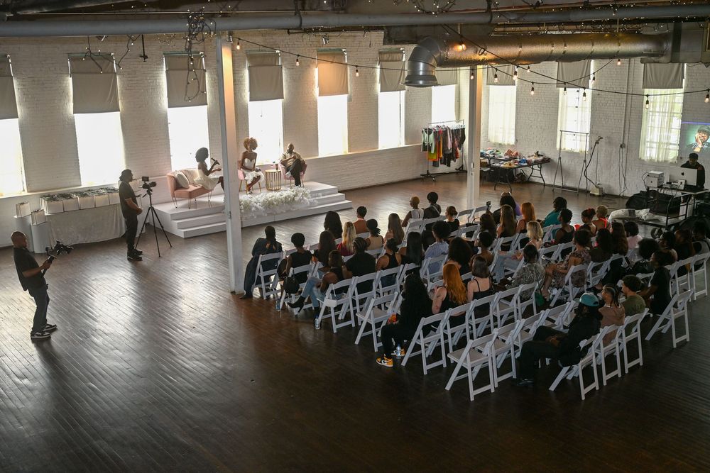 Interior of an event venue with rows of empty white folding chairs set up against a wall with large windows.