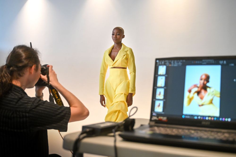 Multiple monitor screens show a professional photo shoot in progress with studio lighting and editing software.