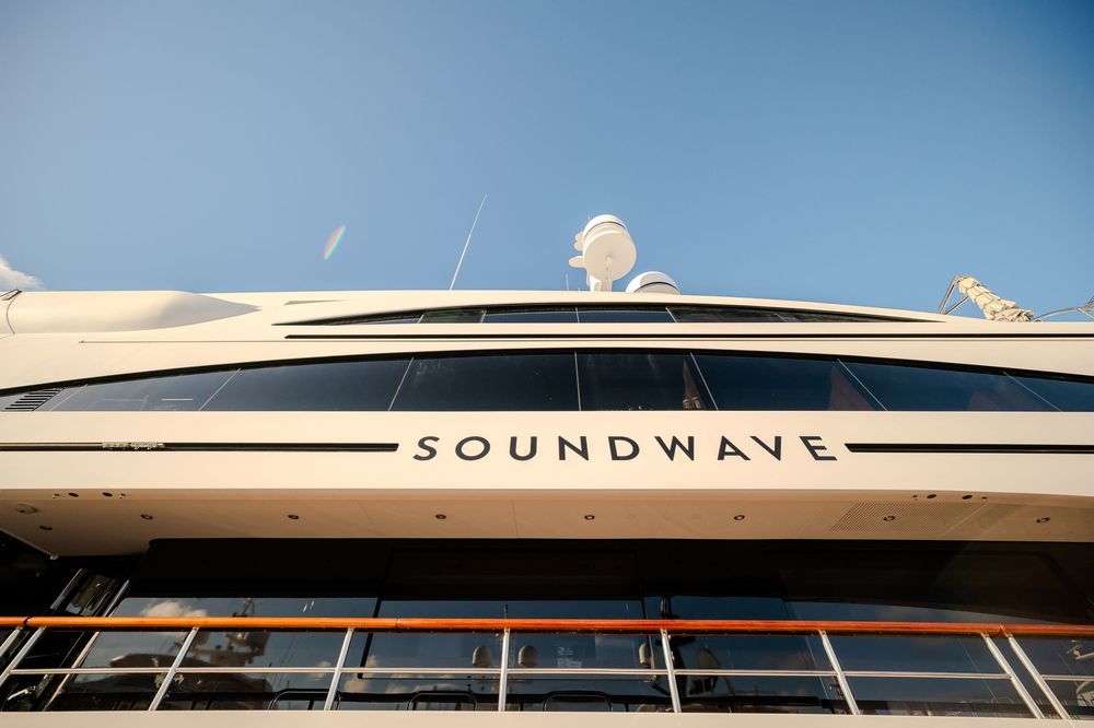 Aerial view of a modern white boat with Soundwave branding cruising through calm blue waters.