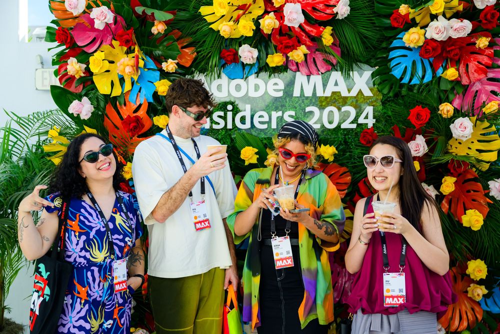 A group of attendees wearing colorful outfits and lanyards pose together against a vibrant floral backdrop.