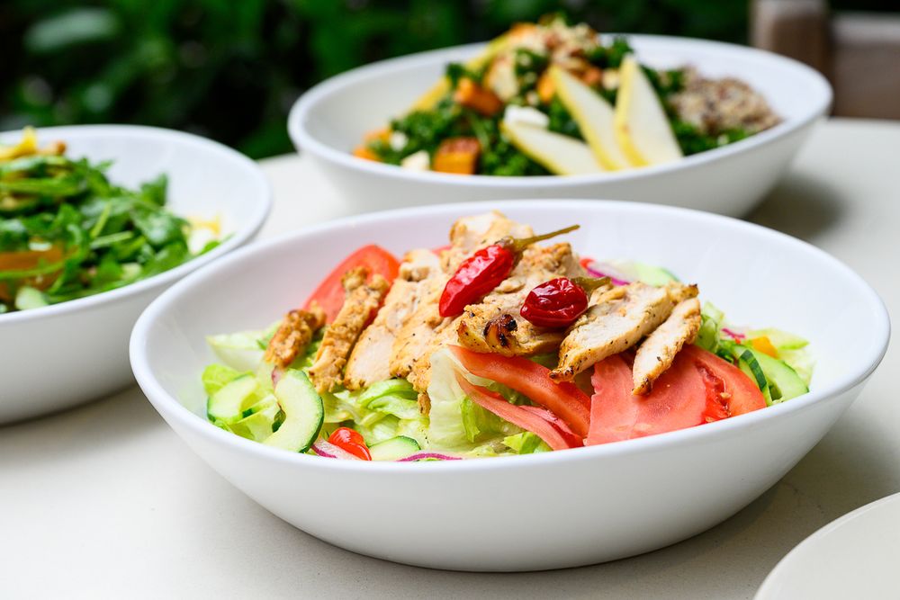 Fresh salads with mixed greens, watermelon, and assorted toppings served in white bowls on a light surface.