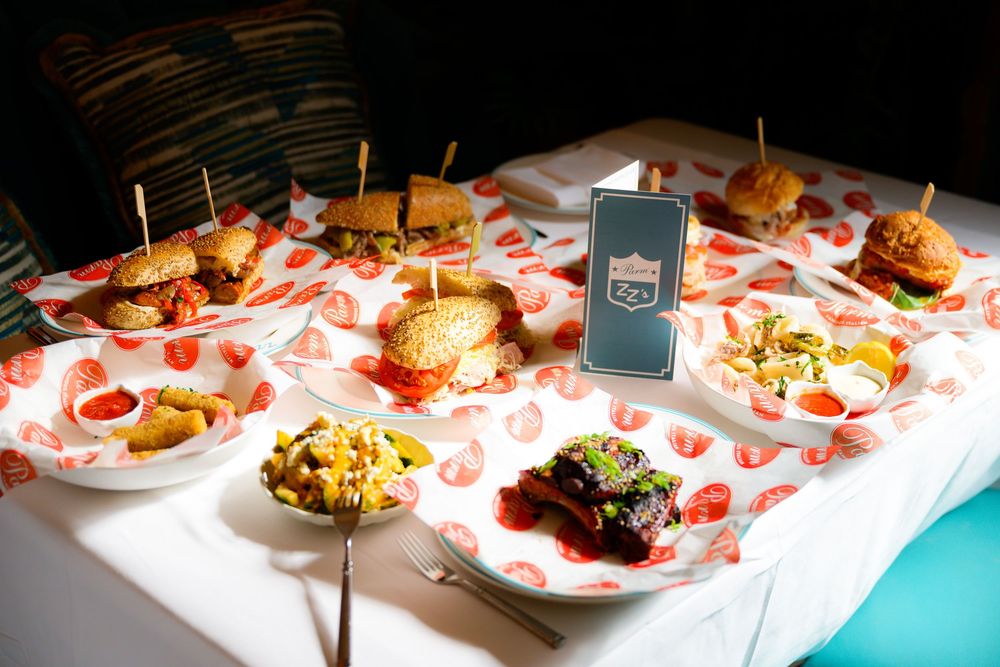 Catered food plates with appetizers and small bites arranged on a white tablecloth with a digital display stand.