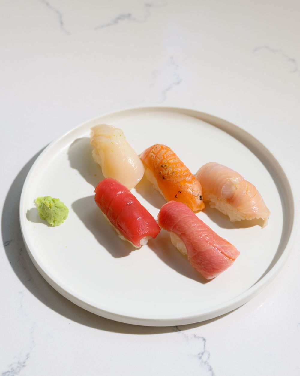 Fresh assorted nigiri sushi pieces including tuna, salmon and white fish arranged on a white plate with wasabi.
