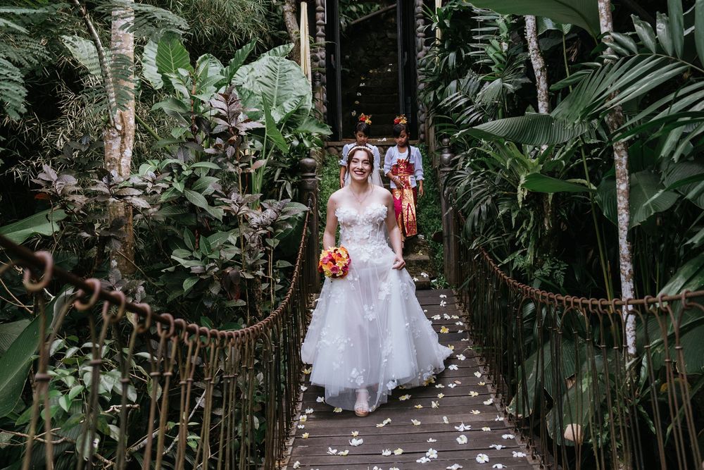 A wedding couple walks down a lush tropical garden pathway lined with palm trees and greenery.