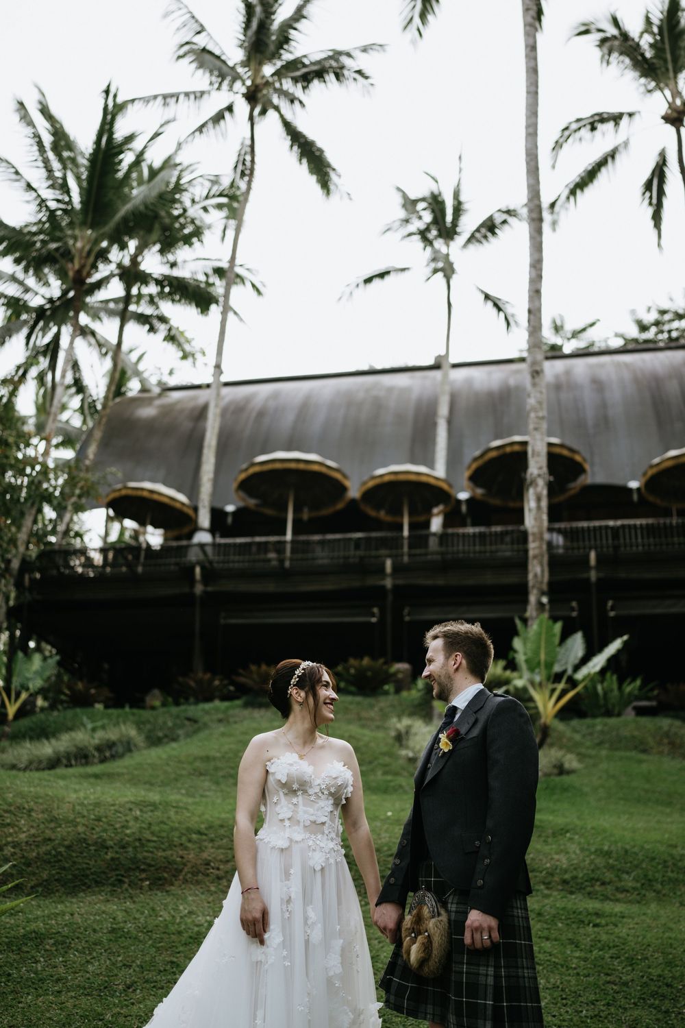 A wedding celebration under tall palm trees with a modern building in the background.
