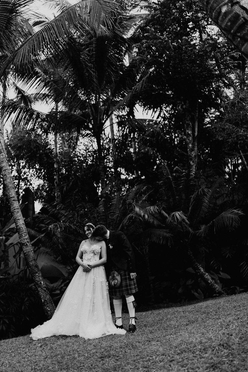 Black and white wedding photos captured in a tropical garden setting with palm trees.