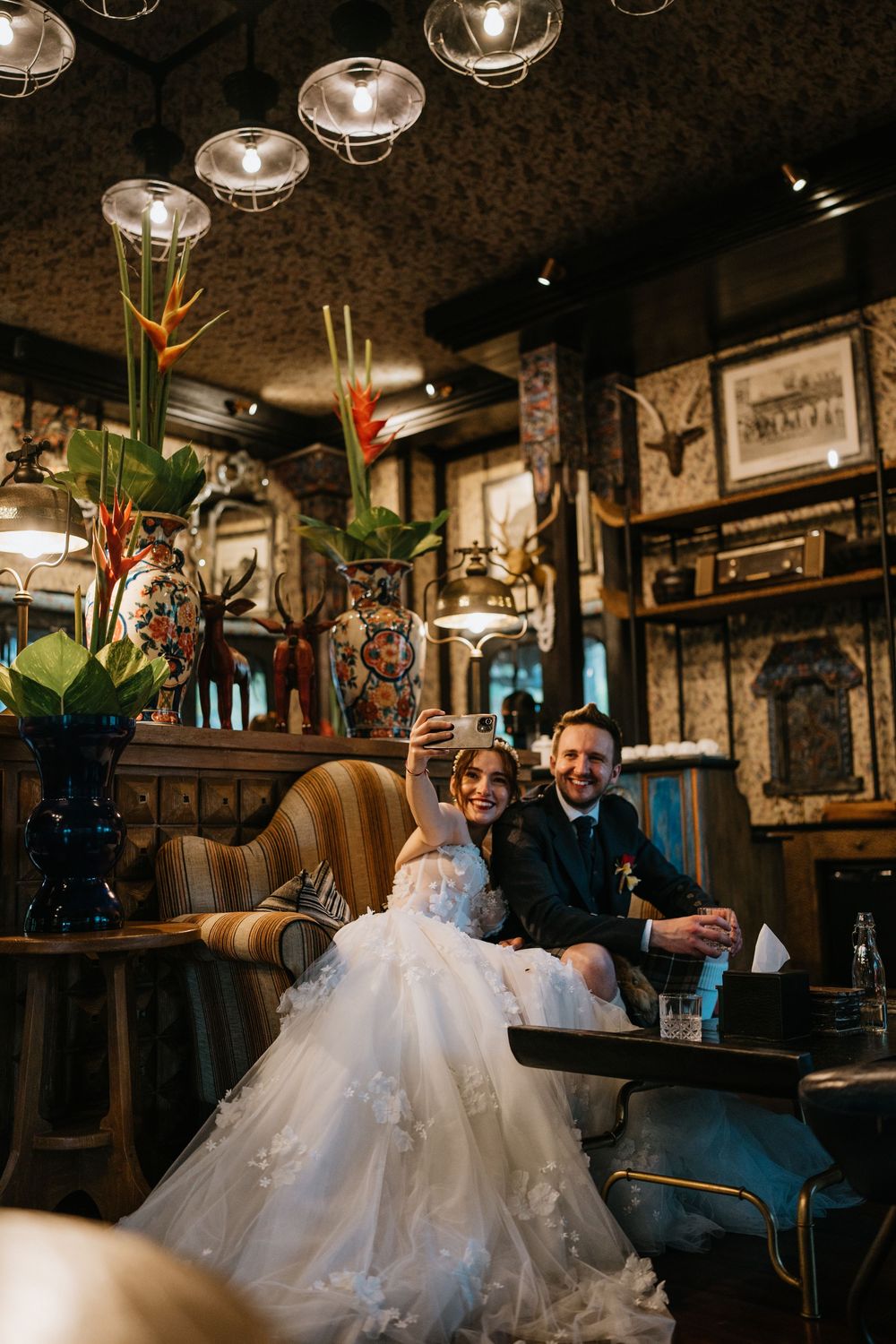 Wedding couple relaxing in a vintage-style bar with ornate decor and mood lighting.