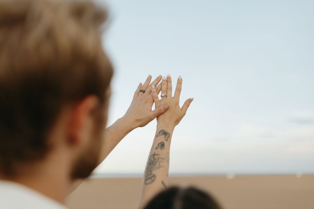 A person reaching their hand up towards the sky with rays of sunlight breaking through the clouds.