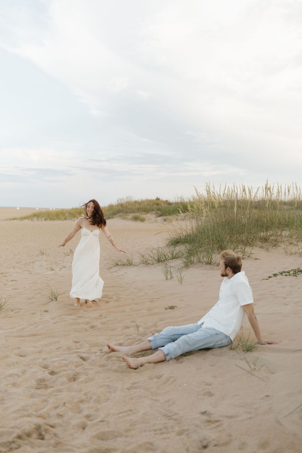 Four candid shots of people laying in the sand at a beach with coastal dunes and grass in the background.