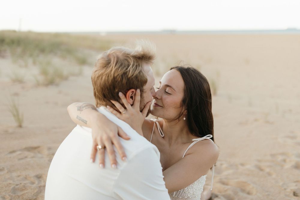 A romantic couple shares an emotional embrace against a sandy beach backdrop during their wedding celebration.