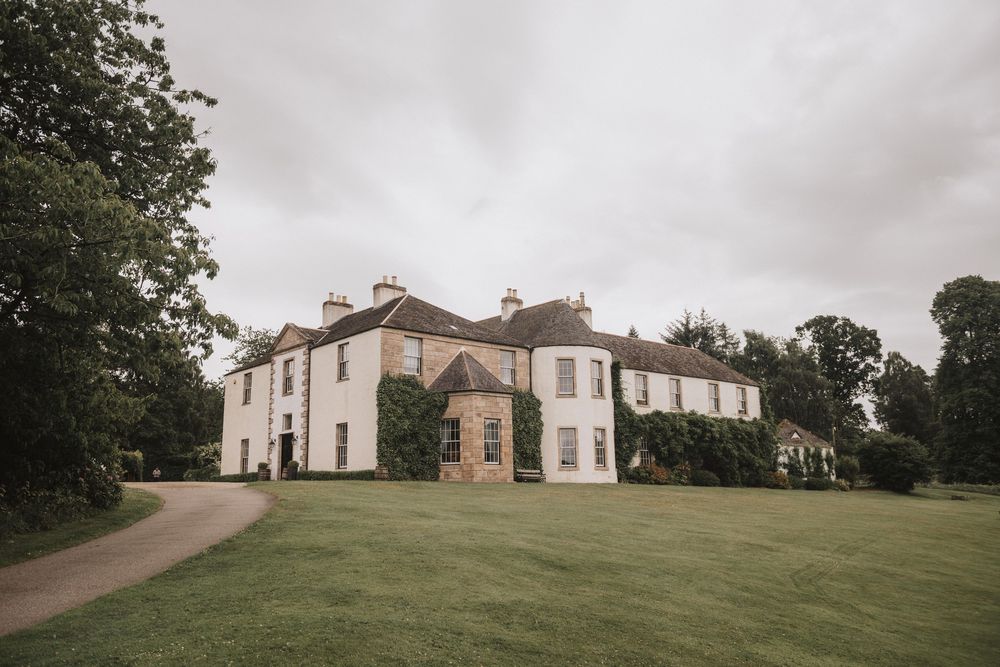 Large historic mansion on a grassy hillside with cloudy skies provides a classic countryside backdrop.