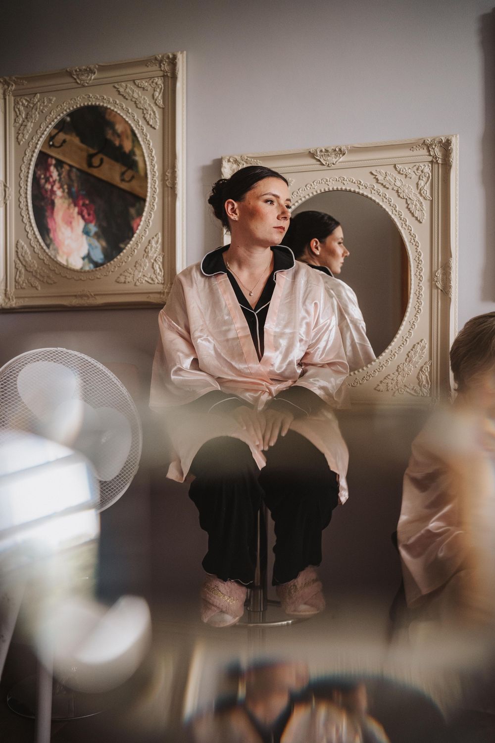 Figure in classical tutu and flowing shirt performs graceful dance movements in an ornate room with decorative wall moldings.