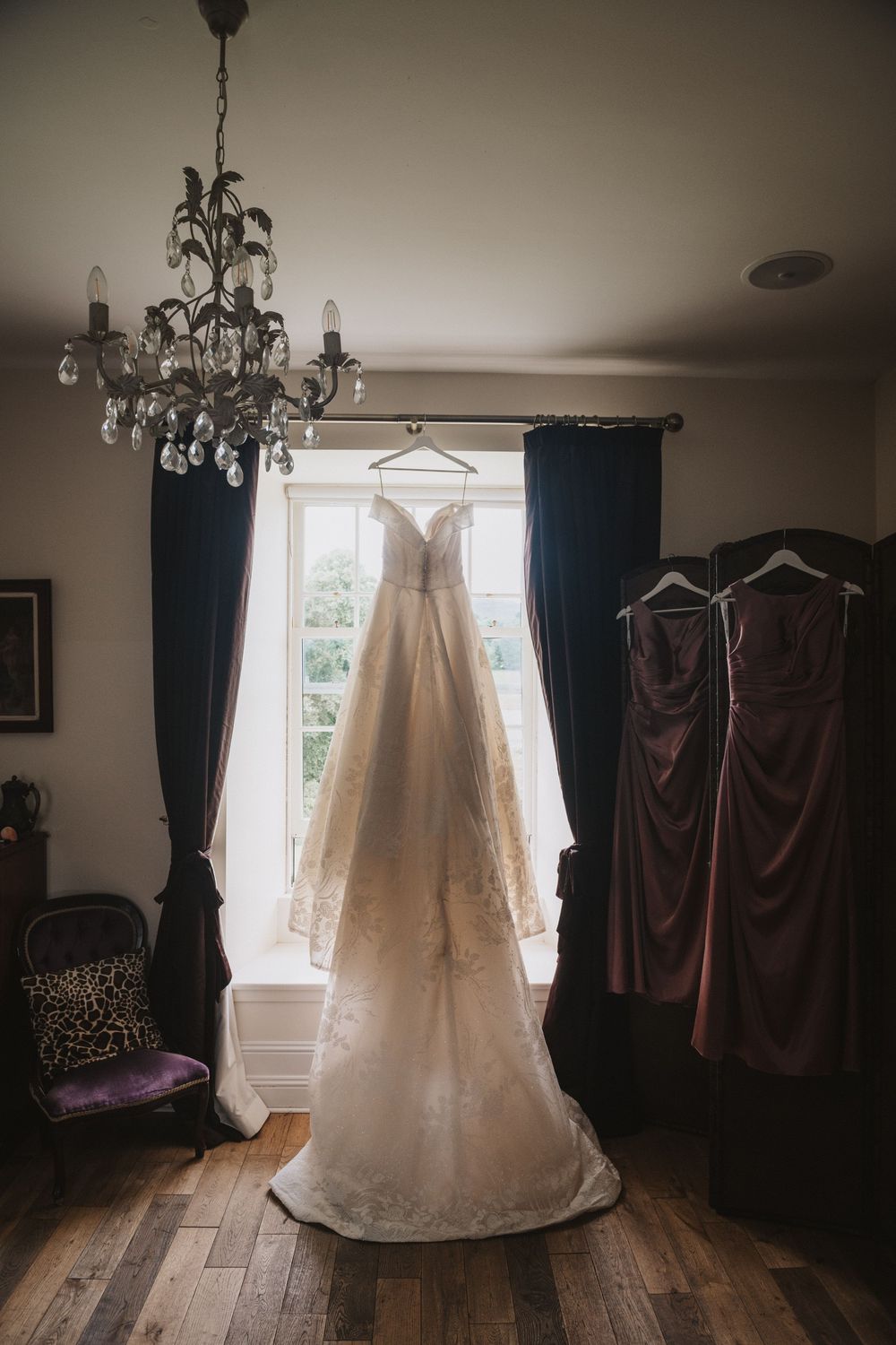 A collection of wedding dresses and formal gowns hanging in a room with dark curtains and crystal chandeliers.