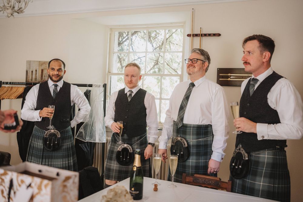 Candid collection of groomsmen getting ready in gray vests and suits in bright indoor venue space.