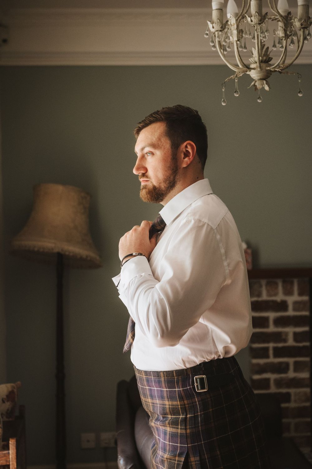 A series of images showing someone getting dressed in formal attire with a plaid kilt against a dimly lit interior backdrop.