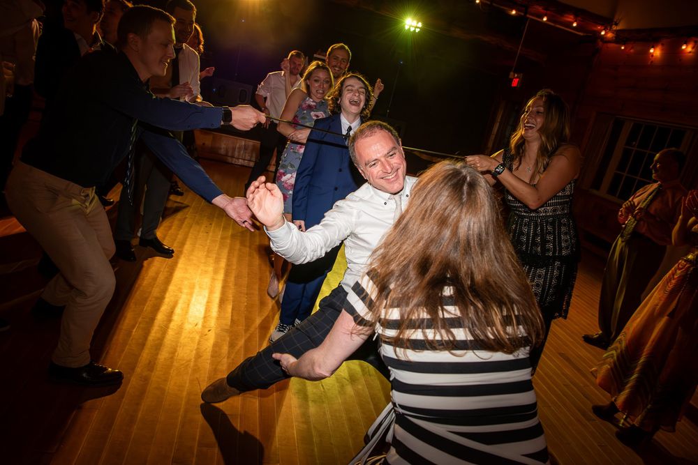 Dancing couples celebrate on a wooden floor illuminated by warm ambient lighting at an evening party.