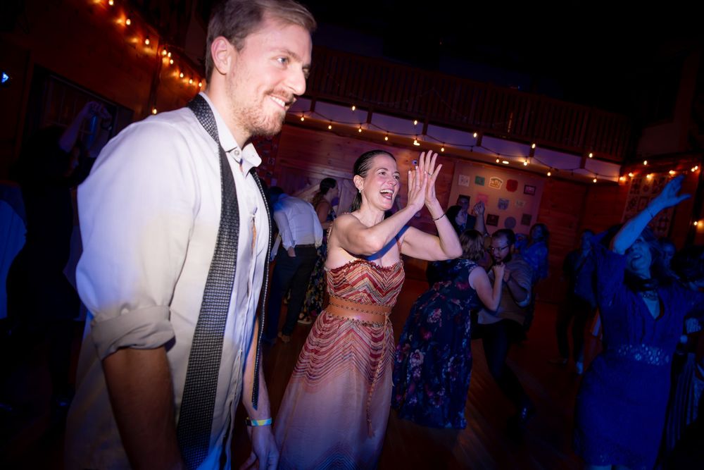 Wedding guests dance and celebrate at a reception party under twinkling lights and blue ambient lighting.