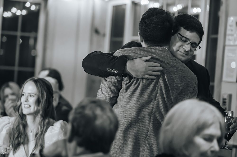 A candid black and white photo of two people embracing at what appears to be a social gathering or event.