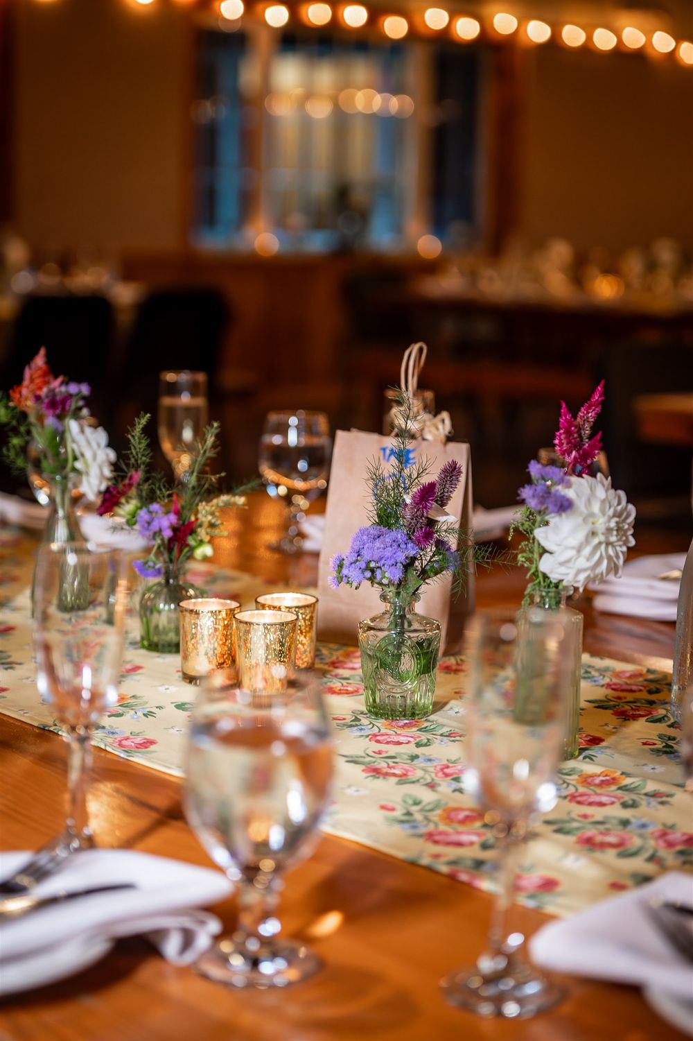 Wooden dining tables adorned with mason jar flower arrangements and tea lights create an elegant rustic reception setting.