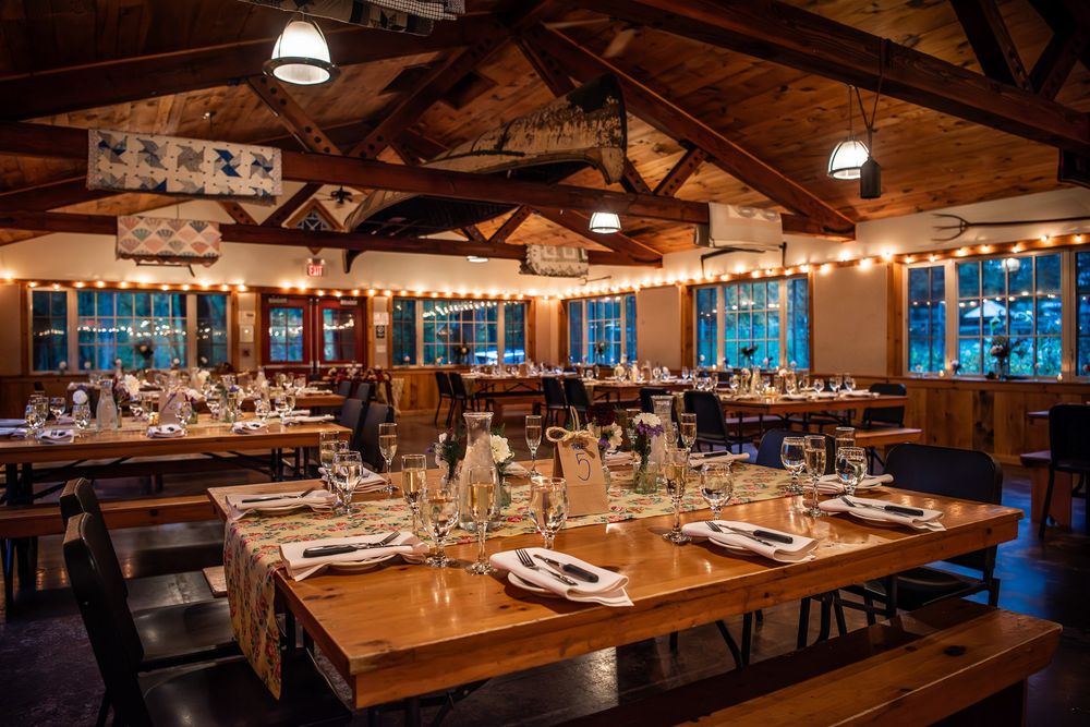 A rustic restaurant dining room with exposed wooden beams and modern lighting features elegant table settings and warm ambiance.