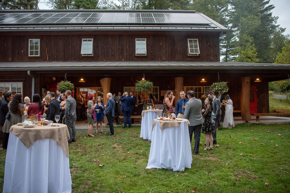 Rustic outdoor wedding reception venue with white tablecloths and guests gathered in a garden-like setting.