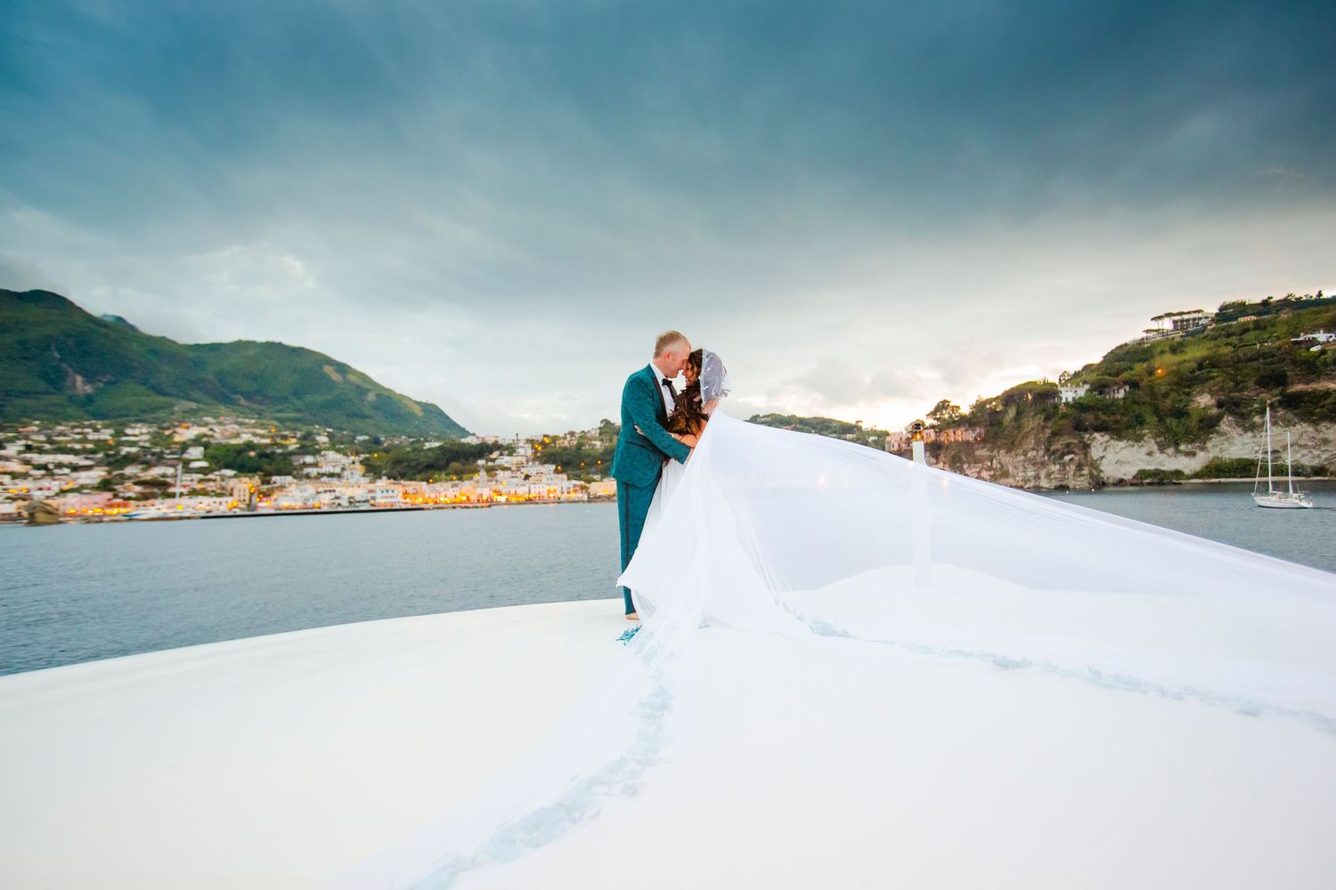 A romantic wedding photo taken on a white surface against a coastal mountain backdrop.
