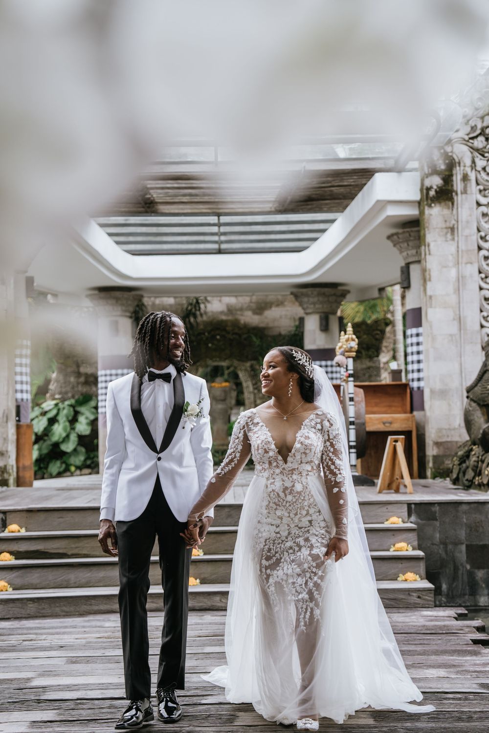 Wedding couple shares candid moments in elegant white attire against modern architectural backdrop.