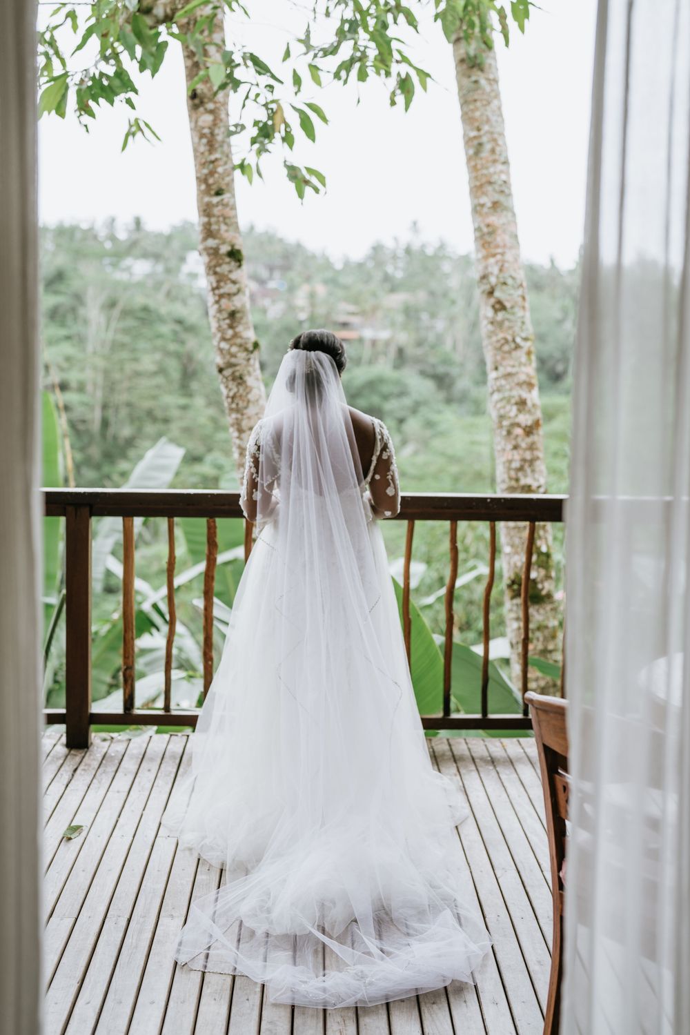 White wedding veil flowing on wooden balcony with tropical forest backdrop.