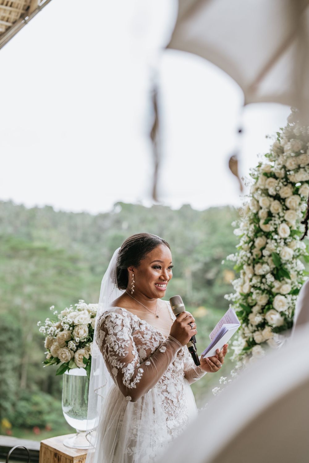 Wedding ceremony setup with white floral arch and tropical landscape views.