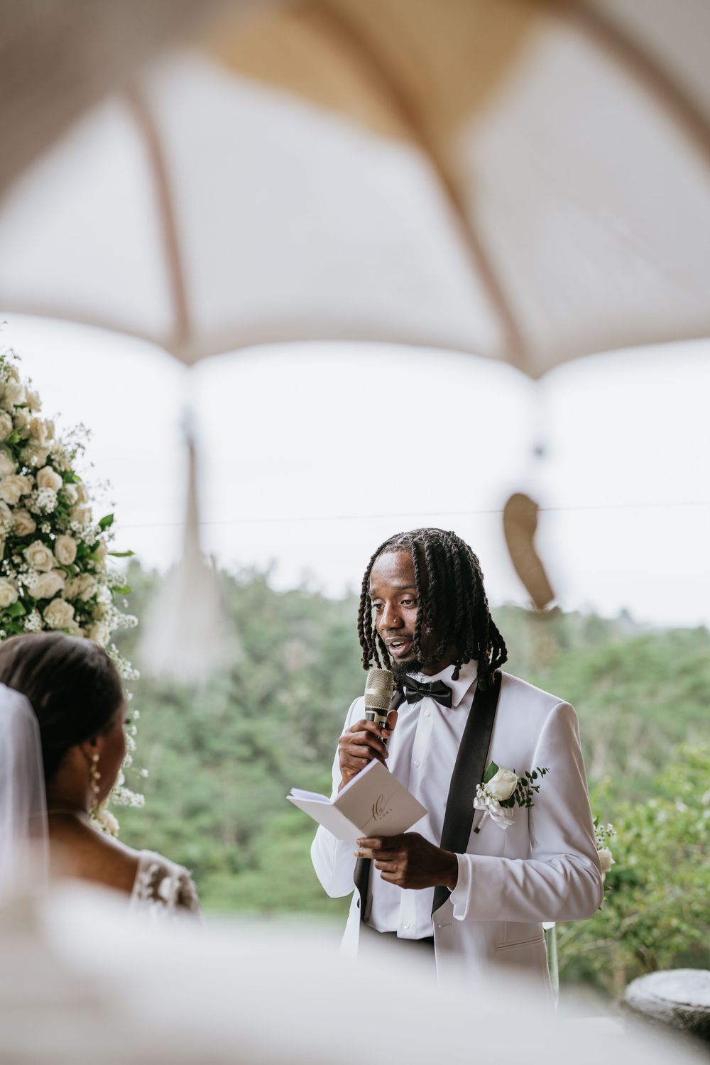 Intimate outdoor wedding ceremony under white umbrellas with floral decorations.