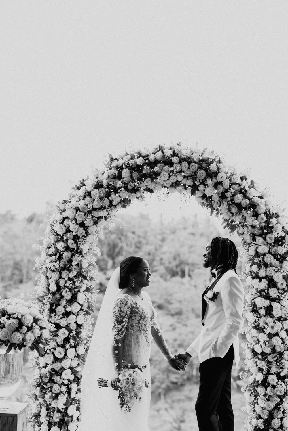 Black and white photo of wedding ceremony under elaborate floral arch.