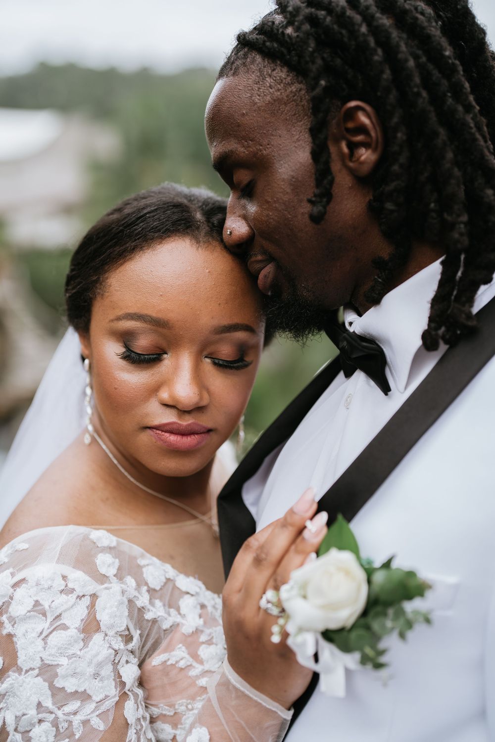 A tender wedding portrait showing a close embrace with the bride in delicate lace and groom in classic tuxedo.
