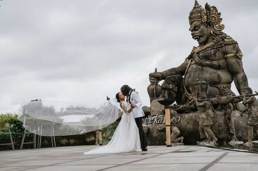 Wedding couple posing dramatically by an ornate stone statue sculpture outdoors.