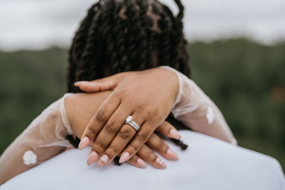 Close-up detail shot of hands with wedding ring and white lace dress fabric.