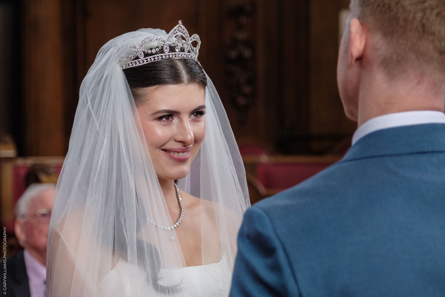 Bride in a flowing white wedding gown and veil smiles during wedding ceremony at church altar.