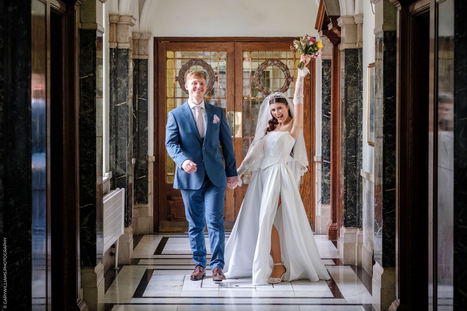 Wedding couple walks with their golden retriever dog through an elegant stone archway corridor.