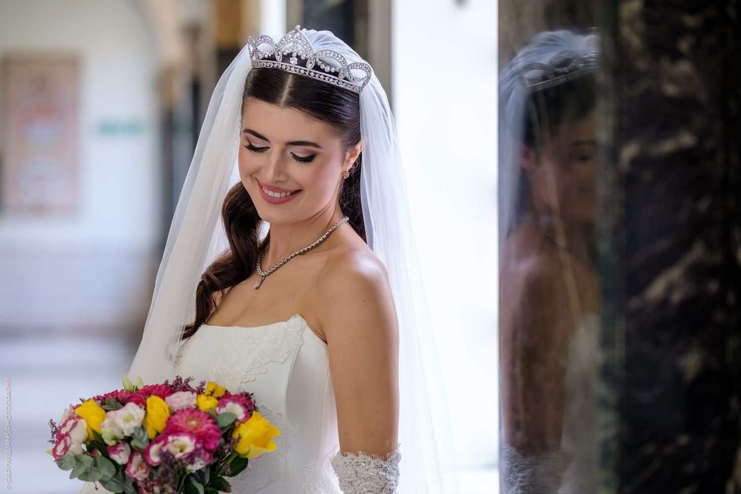Bride wearing white strapless dress and lace veil holds colorful bouquet of tulips and roses on her wedding day.