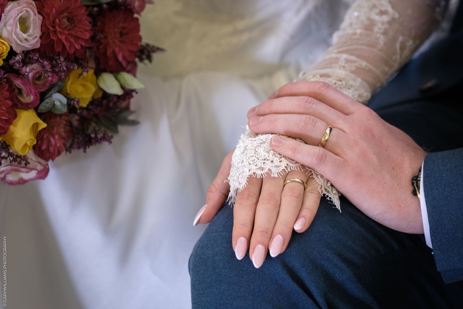 Close-up photo of hands holding sparkly wedding rings against a background of pink and red flowers.