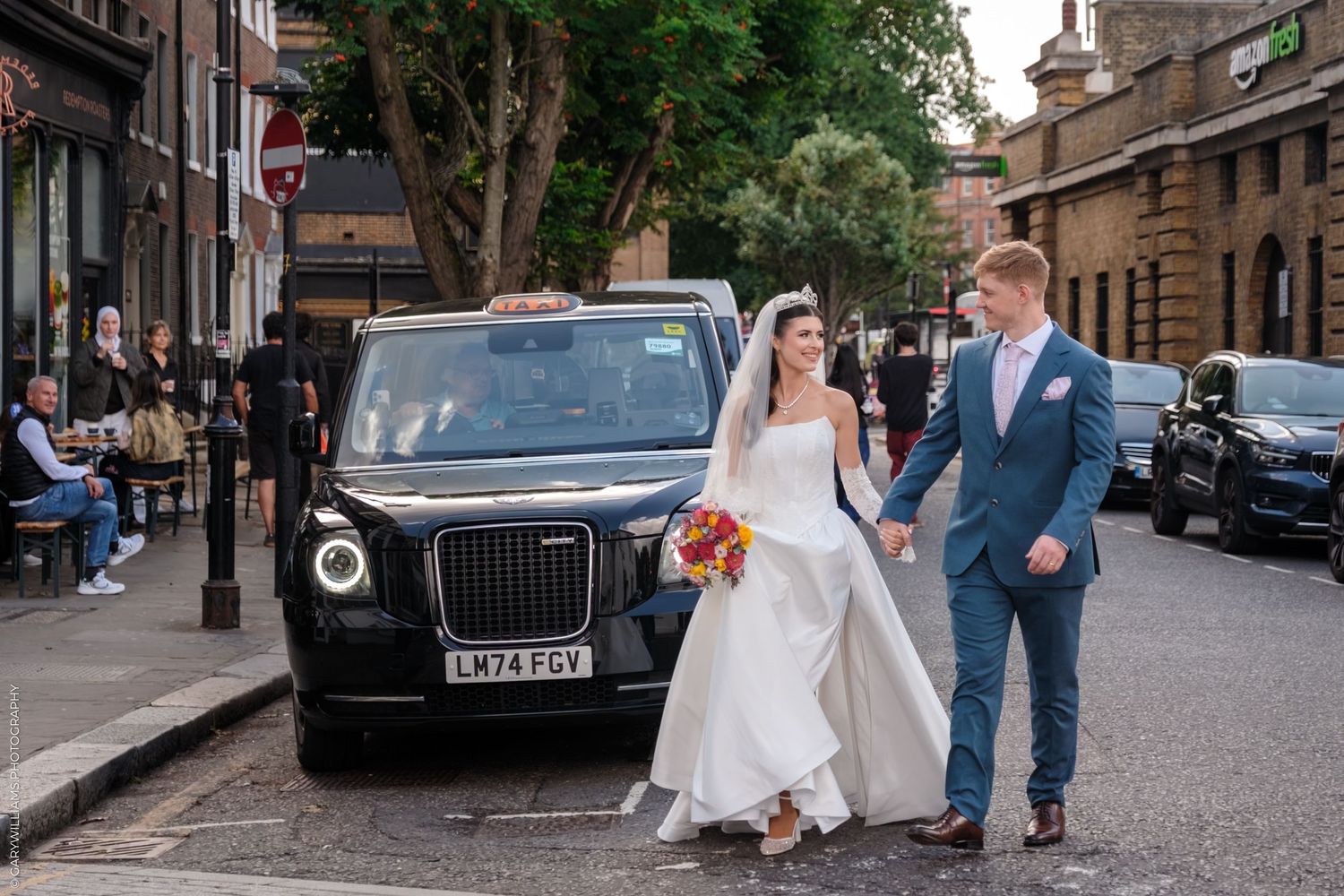 Wedding couple walks down historic cobblestone street with vintage car parked in Edinburgh's Old Town.