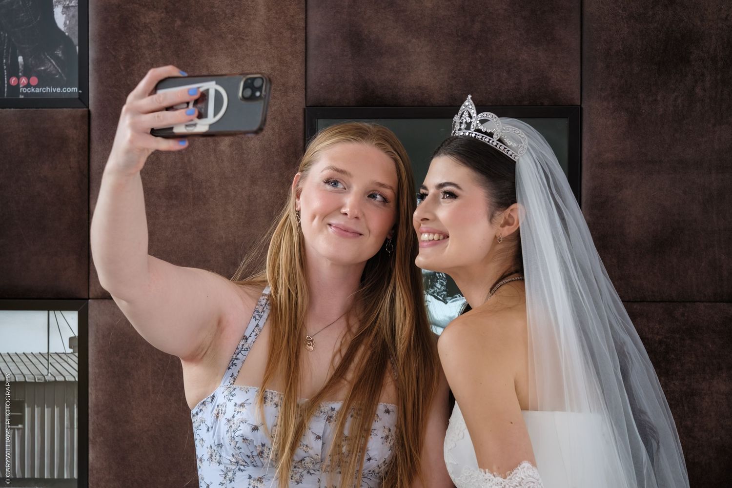 Two women wearing wedding attire take selfies together during a fun bridal photoshoot.