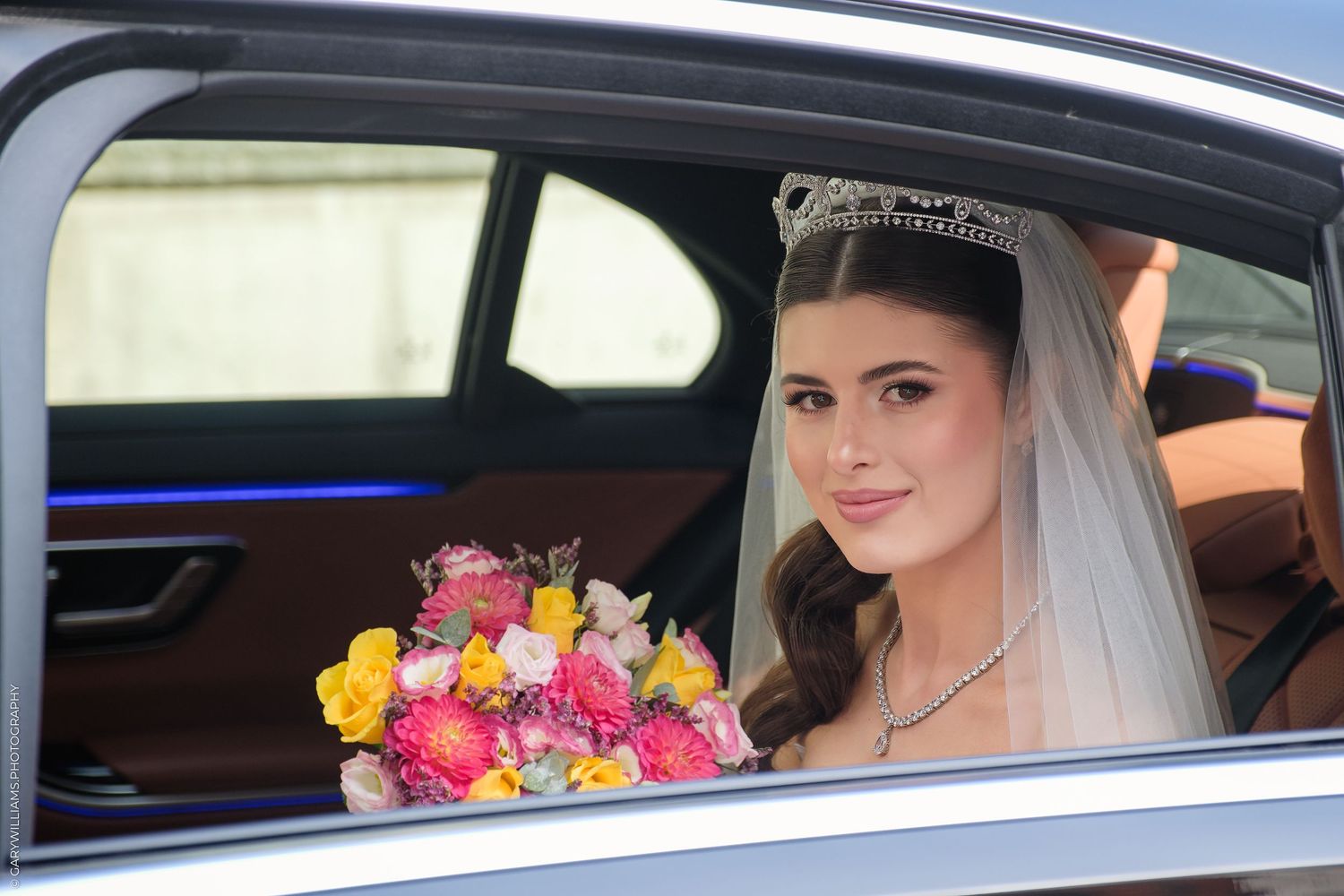 Bride in car window on wedding day with colorful pink and yellow bouquet and veil.