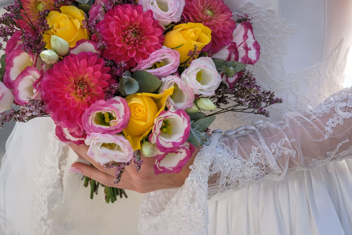 Vibrant pink and yellow floral bouquet with white blooms displayed against a textured lace fabric background.