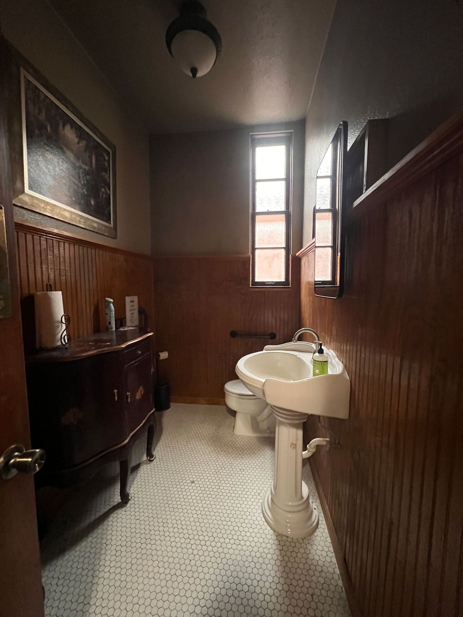Vintage bathroom with dark wood paneling, hexagonal floor tiles, and period fixtures.