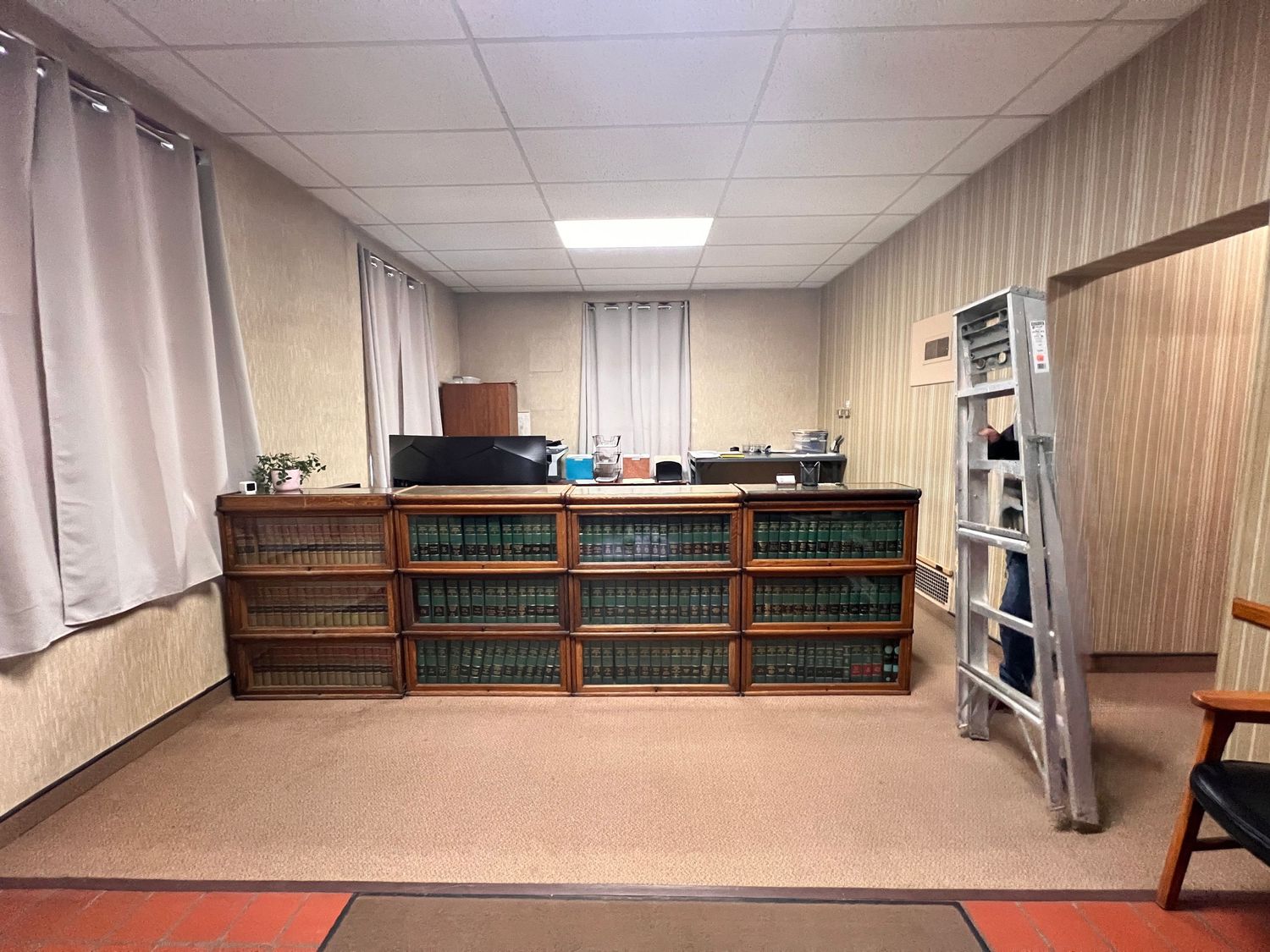 Long interior room with drop ceiling, carpeted floor, and built-in wooden bookshelves along the wall.