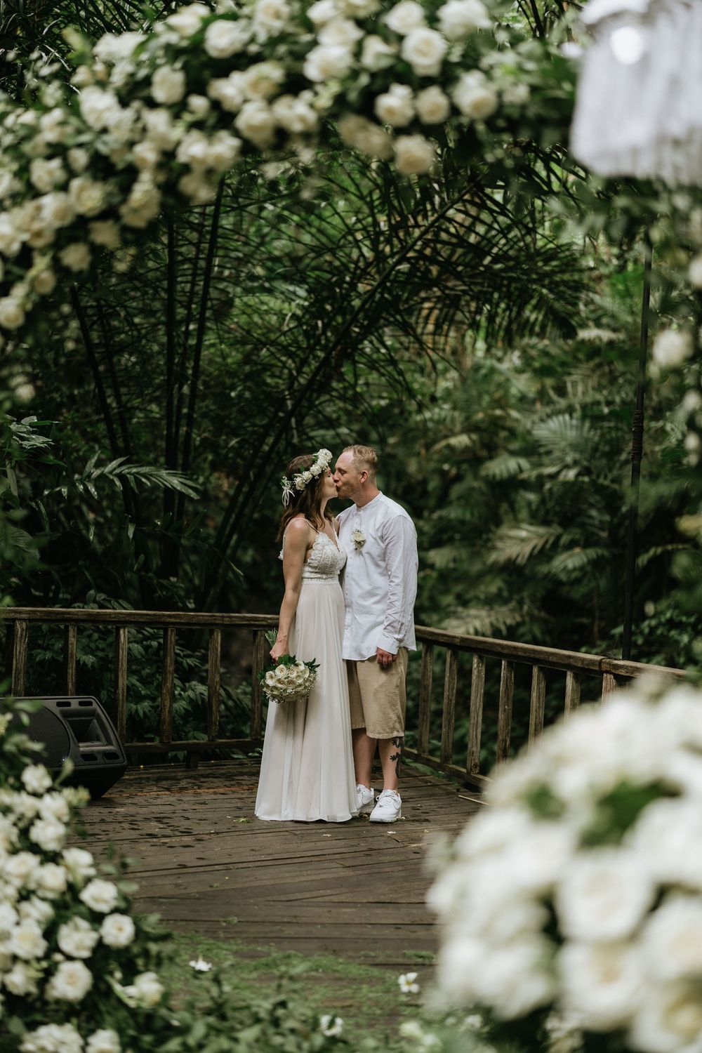Wedding couple sharing intimate moments on a wooden deck surrounded by white roses.