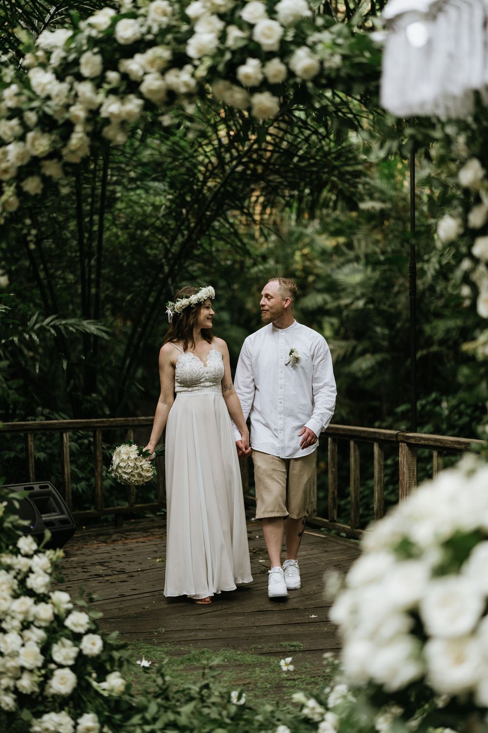 Romantic wedding photos captured on a wooden walkway surrounded by blooming white flowers.