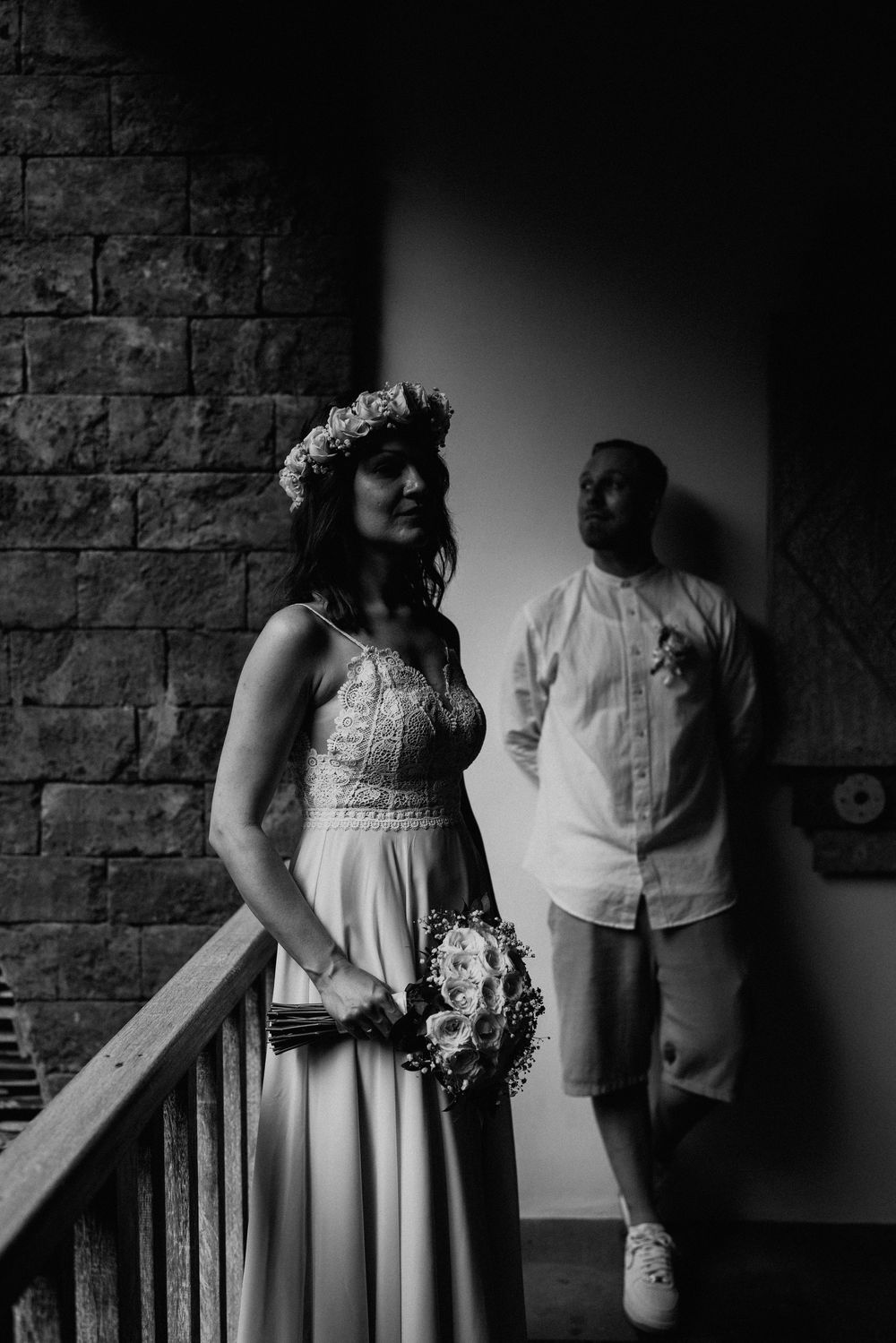 A romantic black and white portrait of a couple in wedding attire against a brick wall.