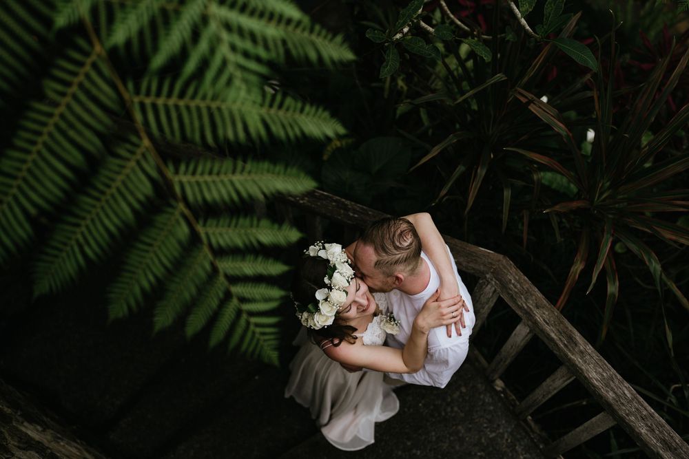 Wedding couple embraces under dramatic tropical foliage.