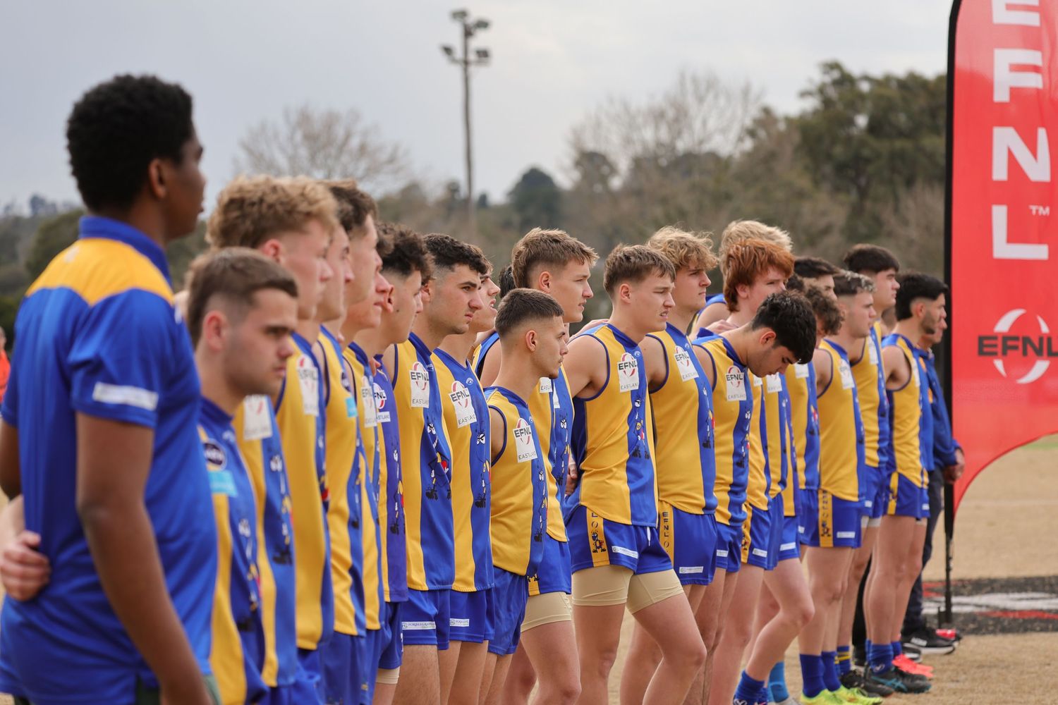 Football players in blue and yellow uniforms stand in line on a field during a pre-game ceremony.