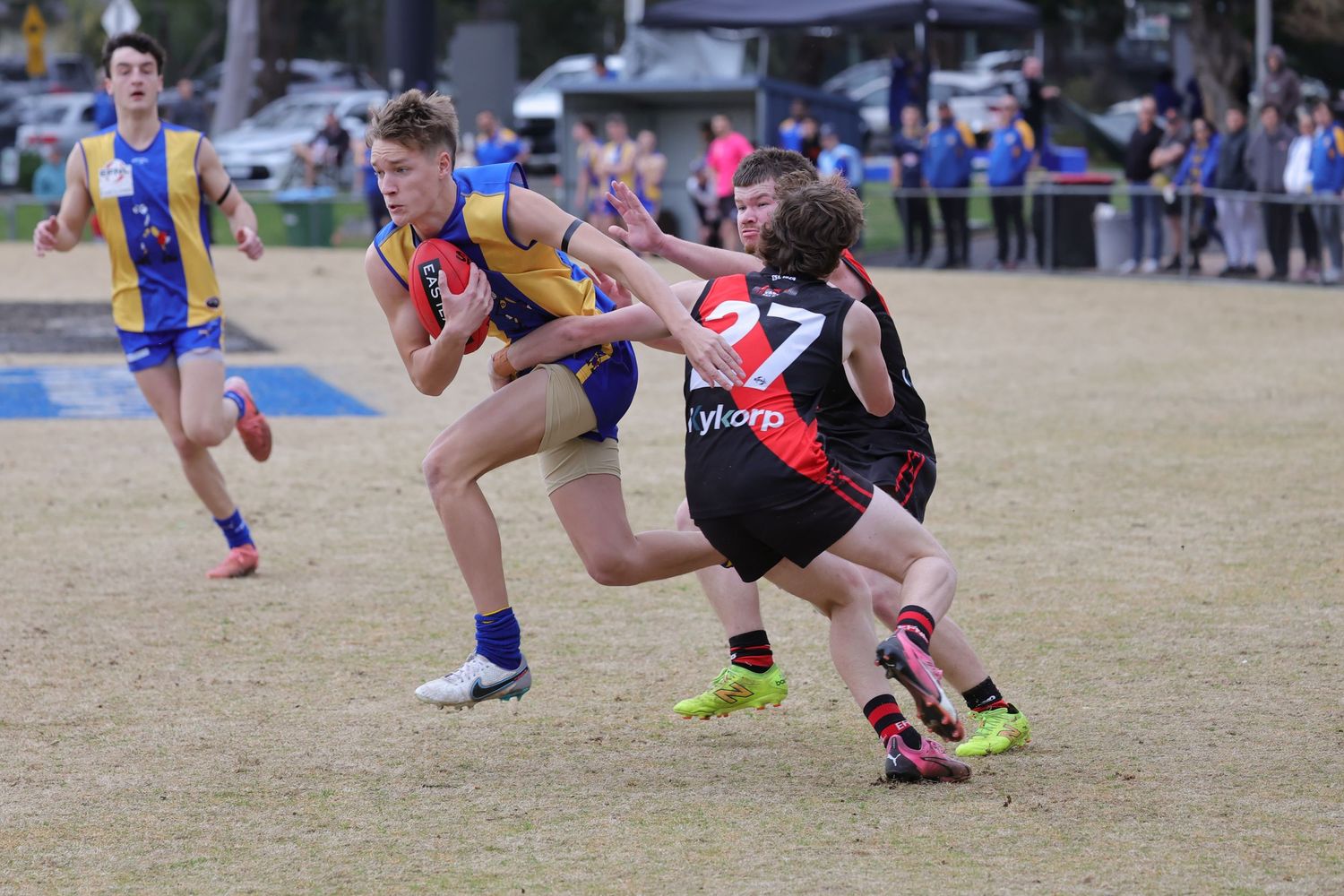 Multiple players compete in a flag football match on a dusty field during a sunny day.